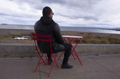 Man sitting on chair looking at sea against sky