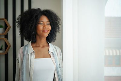 Portrait of young woman standing against window