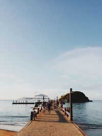 People on pier over sea against sky