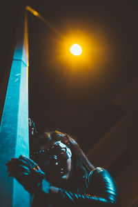 Low angle view of woman wearing mask while standing by illuminated street light at night