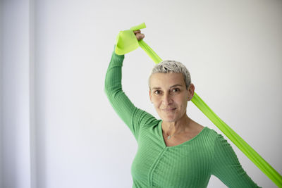 Portrait of young woman with arms raised standing against wall