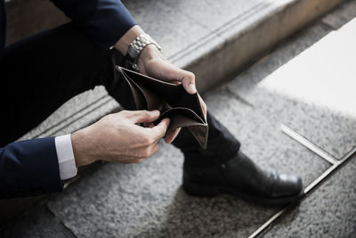 Low section of man holding empty wallet while sitting on floor