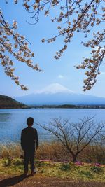 Rear view of man looking at lake against sky