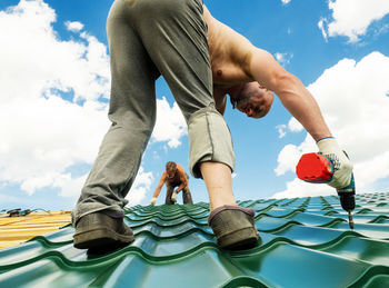 Shirtless men working on roof against sky