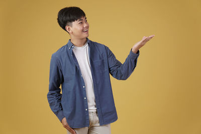 Young man looking away while standing against yellow background