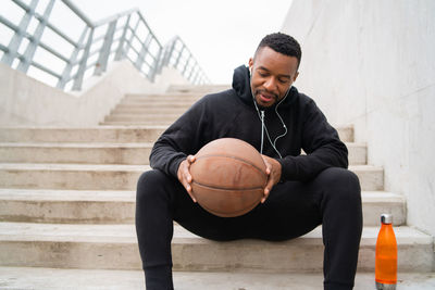 Man holding ball sitting on staircase outdoors