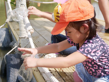 Cute girls wearing cap holding rope sitting on pier by lake