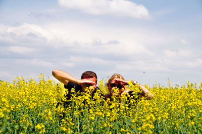 Couple shielding eyes amidst yellow flowers on oilseed rape field