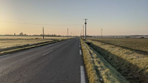 Country road amidst field against sky