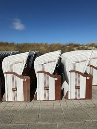 Hooded beach chairs arranged on footpath against blue sky during sunny day