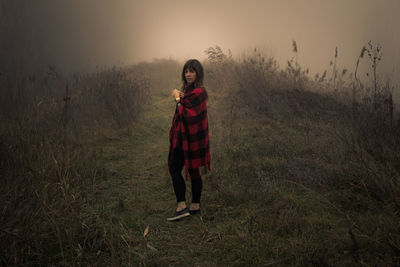 Young woman standing on grassy field during foggy weather