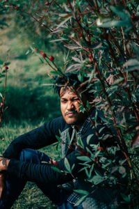 Portrait of young man sitting by plants in forest