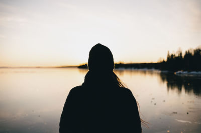 Rear view of silhouette man standing by lake against sky during sunset