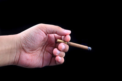 Close-up of hand holding cigarette over black background