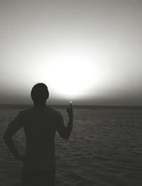 Rear view of silhouette man standing at beach against clear sky