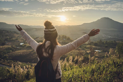 Woman with arms outstretched standing on field against sky