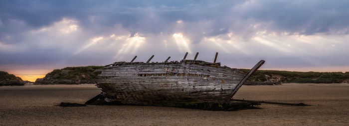 Panoramic shot of abandoned ship on beach against sky during sunset