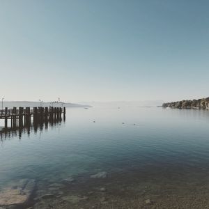 Wooden posts in sea against clear sky