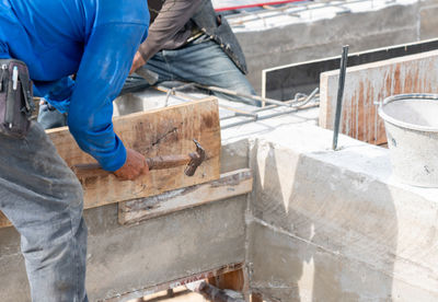 Worker hammering nail on wooden formwork for concrete beam in building construction site.