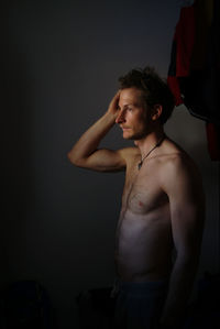 Thoughtful shirtless man standing against wall in darkroom