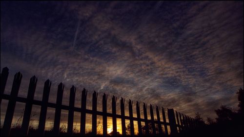 Low angle view of silhouette fence against sky at sunset