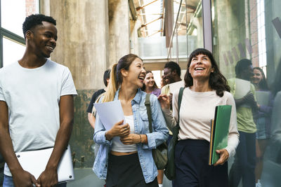 Cheerful multiracial friends talking while walking together in corridor at college