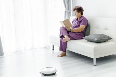 Woman reading book while lying on sofa at home