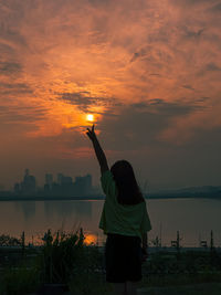 Rear view of woman standing by lake during sunset