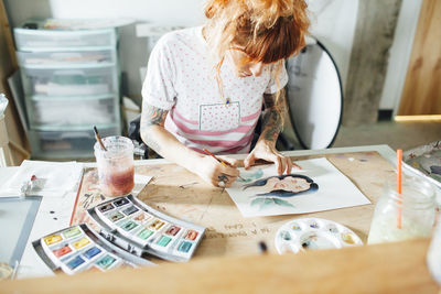 High angle view of artist painting while standing at table in studio