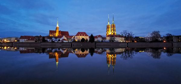 Reflection of illuminated buildings in lake against sky at dusk