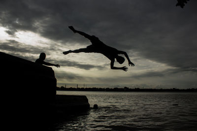 Silhouette man jumping over lake against sky