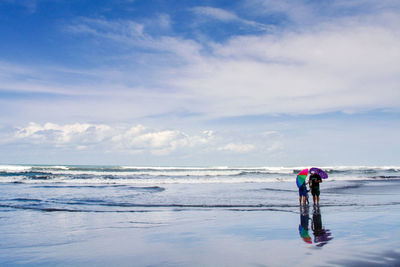 Rear view of women on beach against sky