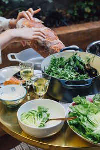 Woman breaking bread at summer evening dinner table with salad, white wine, steamed mussels