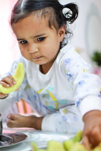 Cute girl eating fruit while sitting on table at home