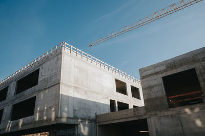 Concrete building and crane at construction site against sky