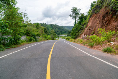 Empty road amidst trees against sky