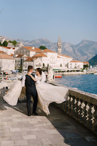 Couple walking in front of buildings against sky