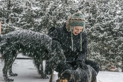 Young woman stroking dogs against plants during snowfall
