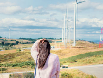 Rear view of woman standing against windmills on landscape