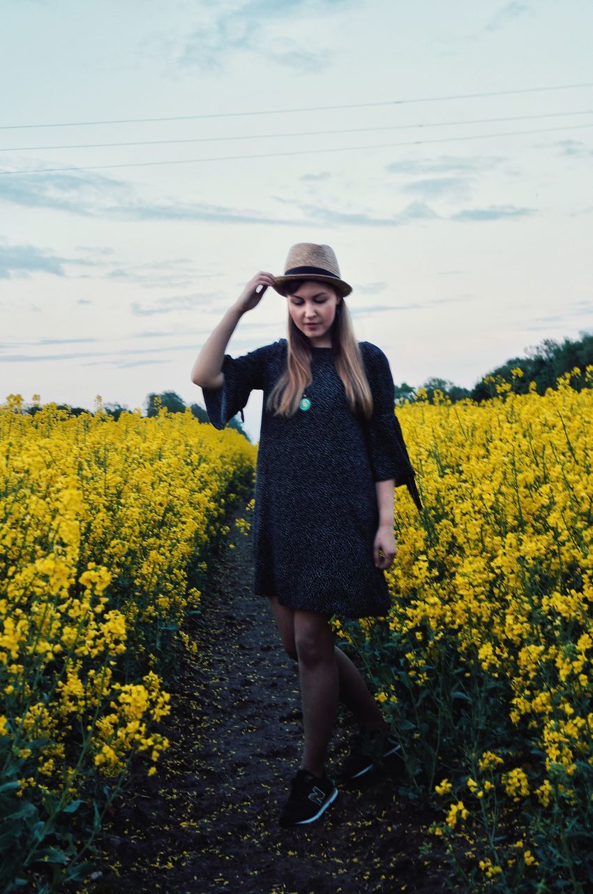 one person, yellow, plant, young women, young adult, field, standing, land, real people, beauty in nature, flower, growth, nature, flowering plant, front view, lifestyles, women, full length, beauty, leisure activity, hair, beautiful woman, fashion, hairstyle, outdoors