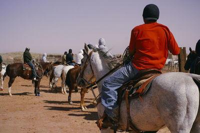 Rear view of men riding horse on desert against clear sky