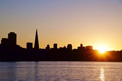 Silhouette city by sea against sky during sunset