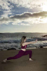 Rear view of woman standing at beach against sky during sunset