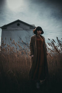 Portrait of young woman standing on field against sky