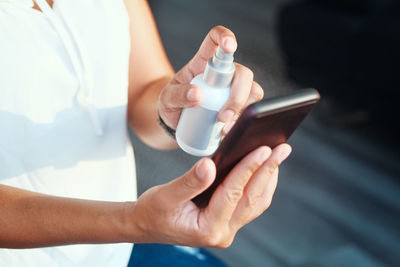 Midsection of woman spraying sanitizer on smart phone