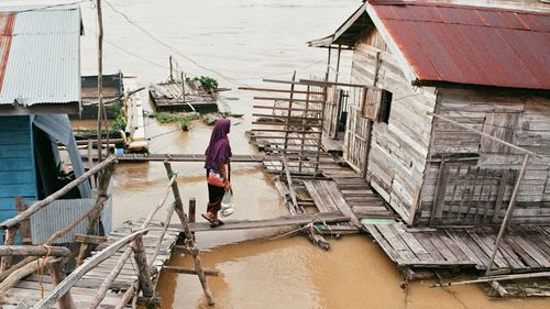 Rear view of man working on canal amidst houses