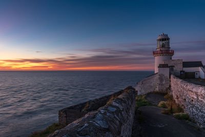 Lighthouse by sea against sky during sunset