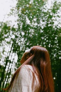 Low angle view of woman looking at trees in forest