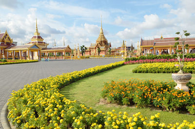 View of flowering plants by building against cloudy sky