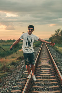 Man standing on railroad track against sky during sunset